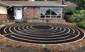 Circular garden labyrinth with brick pathways in front yard of brick house