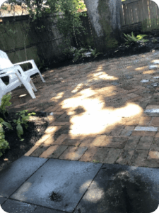 Shaded backyard patio with brick pavers and two white plastic chairs