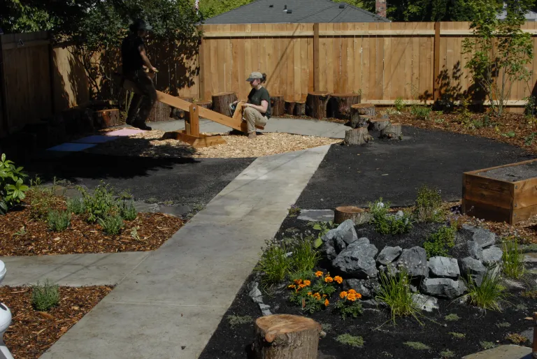 Seattle sustainable backyard with native plant beds, cedar fence, wood seesaw, stone and mulch landscaping