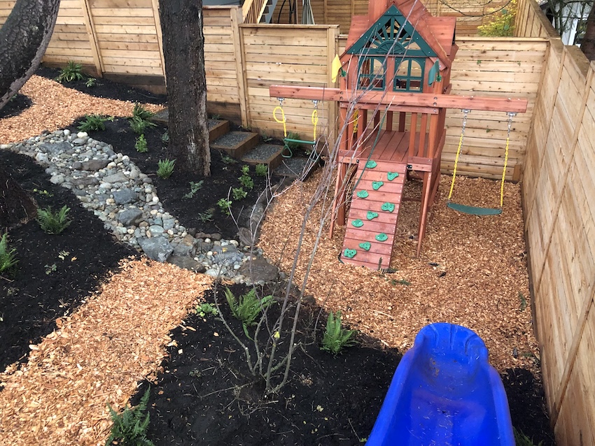 Sustainable backyard playground with wood chips, rock pathway, and wooden fence in Seattle home