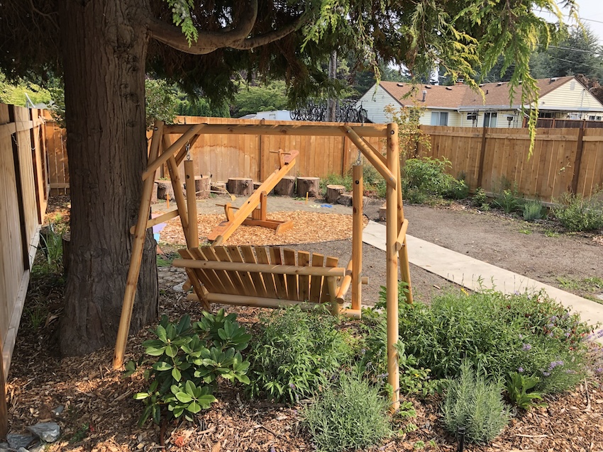 Wooden garden swing set and seesaw in a sustainable landscaped backyard with greenery