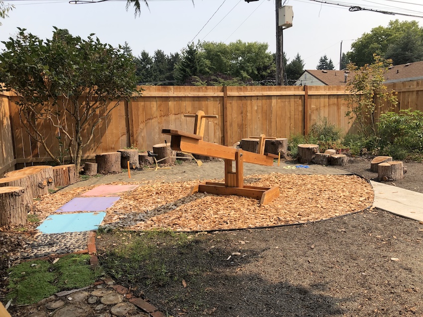 Wooden seesaw and natural playground with mulch and tree stump seating in backyard