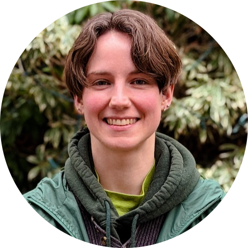 Smiling person with short brown hair wearing a green jacket outdoors